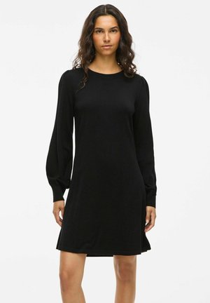 Robe noire en tissu doux, présentant de longues manches bouffantes, un décolleté rond et une coupe décontractée qui tombe au-dessus des genoux.