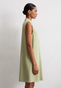 Robe sans manches de couleur vert clair avec une coupe ample, dotée d'un col et de fentes latérales discrètes. Tissu doux avec une texture lisse.