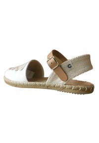 Sandalia de lona blanca con una correa de cuerda beige trenzada y hebilla de cuero marrón. Presenta una suela de yute y un diseño recortado en la punta.