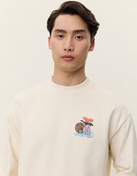 Κρέμα φανελάκι με στρογγυλή λαιμόκοψη που διαθέτει κεντημένο σχέδιο με μια μπάλα μπάσκετ και λουλούδια σε βάζο, τονισμένο με μπλε κύματα.