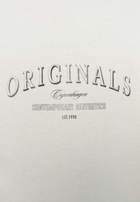 Λευκό βαμβακερό T-shirt με μεγάλο μαύρο τύπωμα που γράφει «ORIGINALS Copenhagen CONTEMPORARY AESTHETICS EST.1990» σε διάφορες γραμματοσειρές.