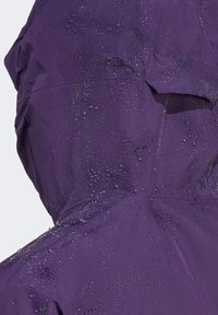 Vodootporna ljubičasta jakna s glatkom teksturom, s vidljivim kapljicama vode na površini i detaljem kapuljače.