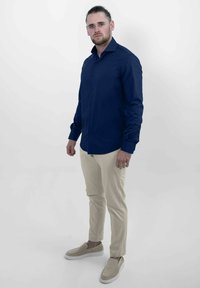 Marineblauwe langemouw knoopshirt, lichtbeige broek en beige instappers, gepresenteerd tegen een neutrale achtergrond.