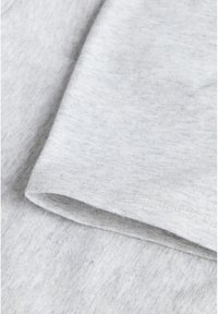Tissu en coton gris clair avec une texture lisse, présentant un bord replié. Un subtil motif chiné est visible à travers le matériau.