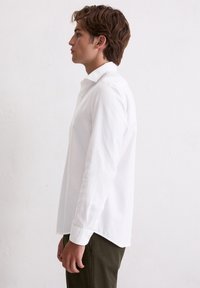 Witte langwerpige blouse met knopen en een klassieke kraag, gladde textuur en een licht gebogen zoom, gecombineerd met olijfgroene broek.