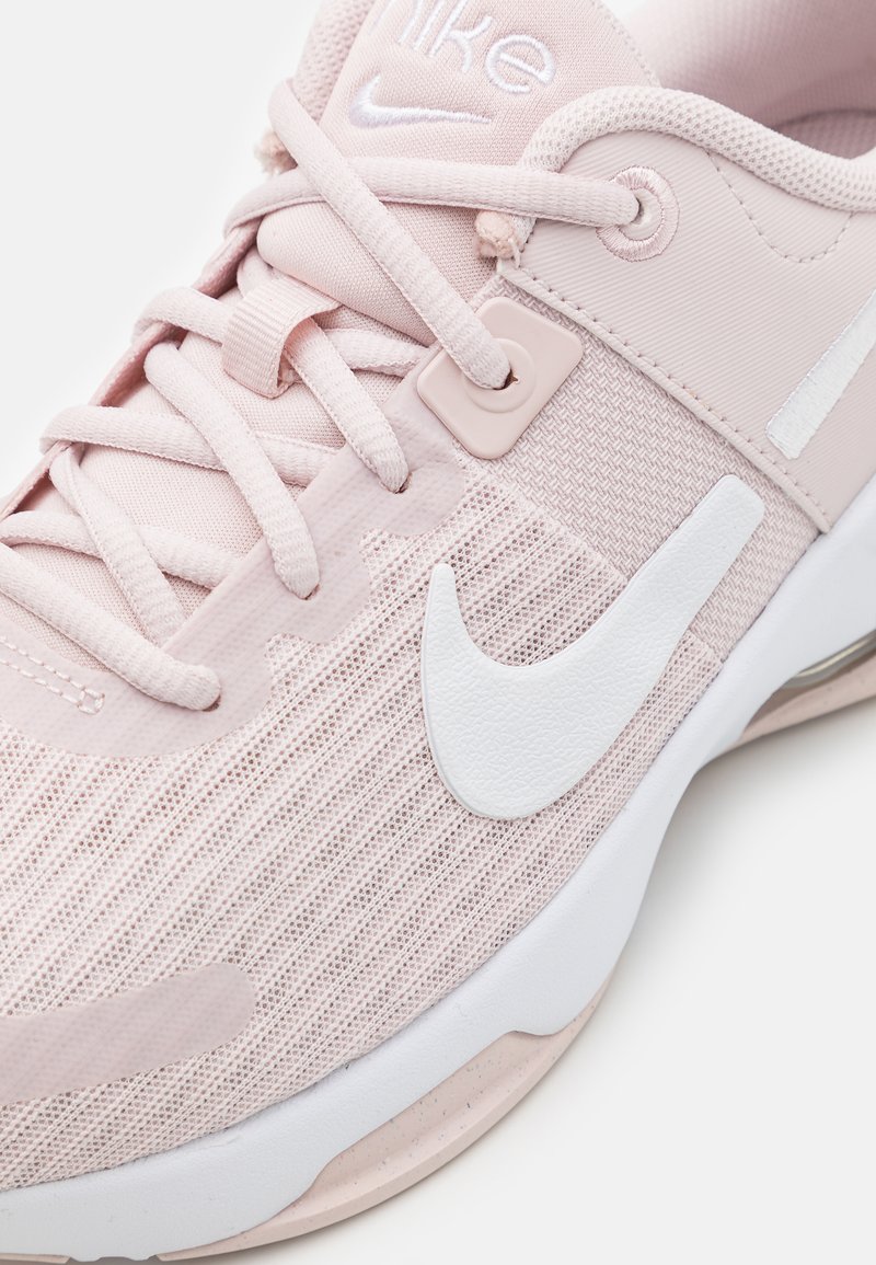 Chaussure de sport rose clair en maille et matériaux synthétiques, avec un swoosh Nike blanc, des lacets plats et une semelle texturée.