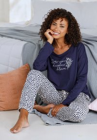 Jūras spēku garām piedurknēm tērps ar baltu ziedu tekstu, apvienots ar baltām biksēm, kas rotātas ar jūras spēku punktiņiem. Mīksts, ikdienas audums; brīvs piegriezums.