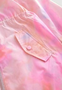 Pink- und lila Batikstoff mit einer Klappe, die mit einem Druckknopf gesichert ist, und einem zusammengefassten elastischen Detail nahe dem oberen Rand.