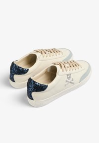 Sneakers in pelle beige con accenti blu glitter sul tallone, striscia laterale azzurro chiaro e lacci beige. Dettaglio con logo di teschio e ossa incrociate.