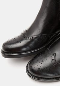 Czarne skórzane botki z ozdobnym przeszyciem typu brogue, z perforowanymi wzorami na czubku i bokach, oraz płaską gumową podeszwą.