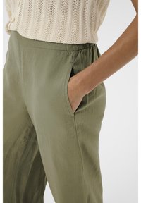 Olijfgroene, lichtgewicht broek van stof met een elastische tailleband en zijzakken. De textuur lijkt soepel met minimale rimpels.