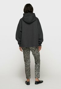 Haut à capuche surdimensionné gris foncé, associé à un pantalon ajusté en imprimé léopard avec des nuances de beige et de noir, porté avec des chaussures plates noires.