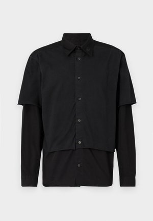 Mustapaita, jossa on kerrokselliset lyhyet ja pitkät hihat. Valmistettu puuvillasta, jossa on klassinen kaulus ja hillitty logoyksityiskohta olkapäällä.