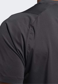 Černé sportovní tričko s krátkým rukávem vyrobené z hladké, lehké tkaniny; má bezešvou konstrukci ramen a jemný lesk na povrchu.