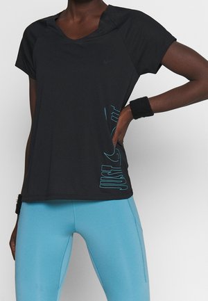 Personne portant un t-shirt noir à manches courtes avec un texte bleu "Just Do It" et des leggings bleu vif, avec des bracelets noirs aux deux poignets.