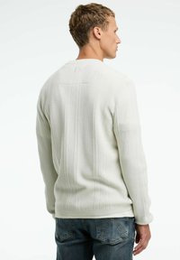 Witte trui met gestructureerde zigzag- en verticale streeppatronen. Heeft een ronde hals en ribbelmanchetten, gecombineerd met blauwe denim jeans.