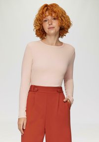 Lichtroze geribbelde top met lange mouwen gecombineerd met hoog-waisted roestrode broeken met knoopaccenten en zijzakken.