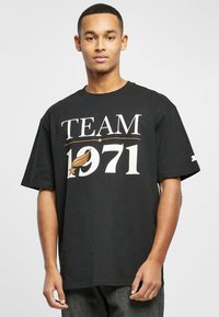 Tricou oversized negru cu text grafic alb și aurie "TEAM 1971" în centru. Manșete scurte, material din bumbac, decolteu rotund.