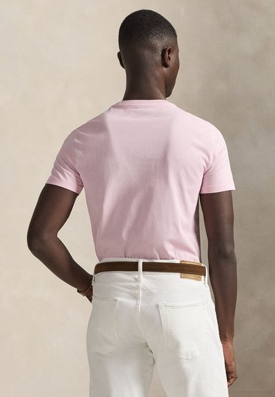 Ροζ κοντομάνικο t-shirt από βαμβάκι, με στρογγυλή λαιμόκοψη και λεία υφή, συνδυασμένο με λευκά τζιν και καφέ δερμάτινη ζώνη.