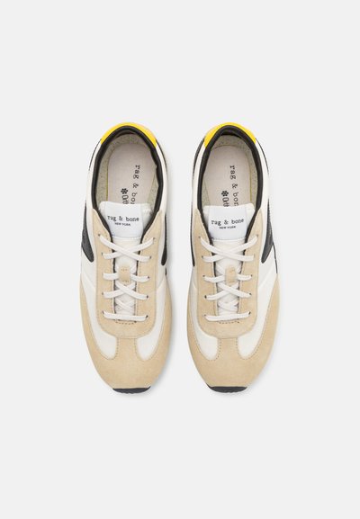 Athletic sneakers in beige and white suede and leather, featuring black accents, white laces, and a yellow collar detail.