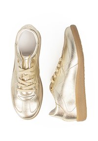 Zapatillas metálicas doradas con un acabado de textura suave, punta redonda y suela de goma. Presentan cordones beige y detalles de costura en contraste.