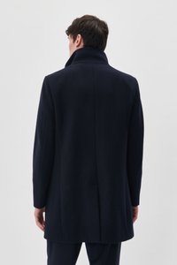 Marineblå uldfrakke med høj krave, lange ærmer og skræddersyet pasform. Glat tekstur og minimalistisk design uden synligt hardware eller pynt.
