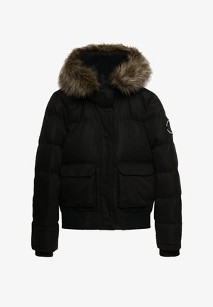 Chaqueta acolchada negra con capucha forrada de piel, dos bolsillos frontales, puños acanalados y cierre frontal con cremallera. Textura suave, diseño aislante.