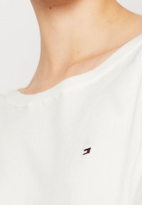 Haut en coton blanc tricoté avec un col rond et des manches courtes. Présente un petit logo brodé en rouge, blanc et bleu sur la poitrine.