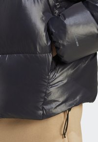 Puffet, mørkeblå jakke med skinnende overflade, elastiske manchetter og snor i kanten. Har et lille logo på ærmet og en lynlåslomme.