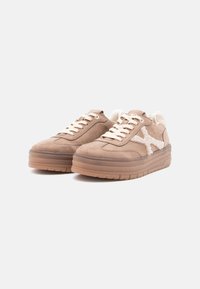 Bruine suède sneakers hebben een textuurdesign, crèmekleurige veters en een witte fluweelachtige accent. De zool is dik en heeft een kauwgomkleur.