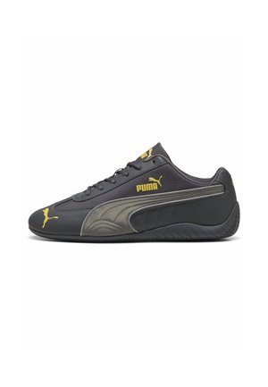 Zwarte Puma lage sneaker met grijze zijstreep en gele Puma-logo accenten op de neus, zijkant en tong.