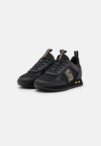 Zapatillas deportivas negras con parte superior de malla, acentos dorados, suela texturizada y branding. Tienen un diseño elegante y moderno con materiales contrastantes.
