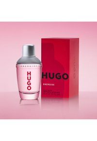 Hugo Energise eau de toilette 75 ml flaske med sølvkork ved siden av en rød rektangulær eske på en rosa reflekterende overflate.
