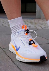 Hvit idrettssko med blå swoosh-design, oransje detaljer og teksturert mesh-overdel; har et unikt snøresystem og polstret såle.