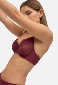 Sujetador de encaje y tela burdeos con copas estructuradas, intrincado patrón de hojas, tirantes ajustables y una banda inferior ancha.