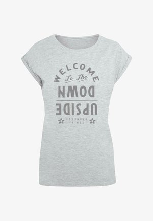 Pelēks kokvilnas T-kregs ar ruļļveida piedurknēm. Uzraksts "LAIPNI LŪDZAM APVIRTĪTĀ PASAULĒ" tumši pelēkā krāsā un zem tā "STRANGER THINGS".