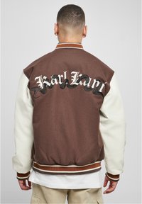 Brun bomberjacka med vita ärmar, med "Karl Kani" i vitt och svart orm mönster på baksidan, ribbade ärmslut och nederkant.
