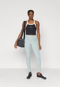 Juodas trumpas viršus su baltais dirželiais, šviesiai žali kelnės ir juodi sportbačiai. Papuošalai apima mažą juodą rankinę su petnešomis.