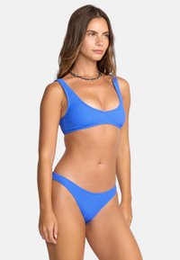 Ribkowany niebieski bikini z trójkątnym stanikiem i regulowanymi ramiączkami. Dół ma niską talię, co doskonale uzupełnia design góry.