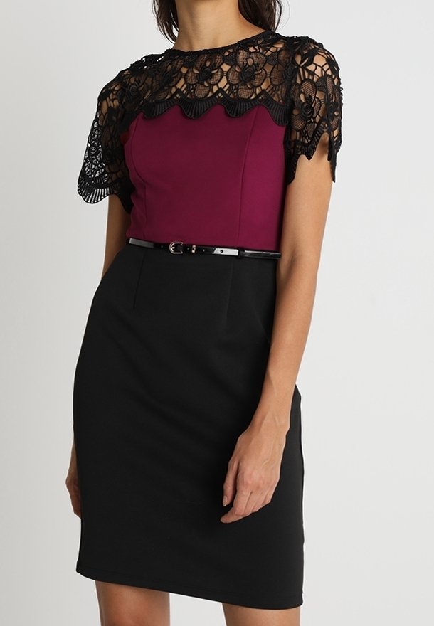 Enges Kleid mit einem Pflaumenoberteil und schwarzem Spitzenoverlay, das einen gewellten Ausschnitt aufweist. Ein schwarzer Stoffgürtel sitzt an der Taille. Strukturiertes Spitzen-Detail.