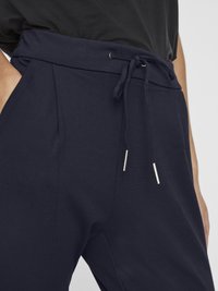 Navy blue jogger pants with a drawstring waist, featuring silver metal tips, side pockets, and a soft, textured fabric.