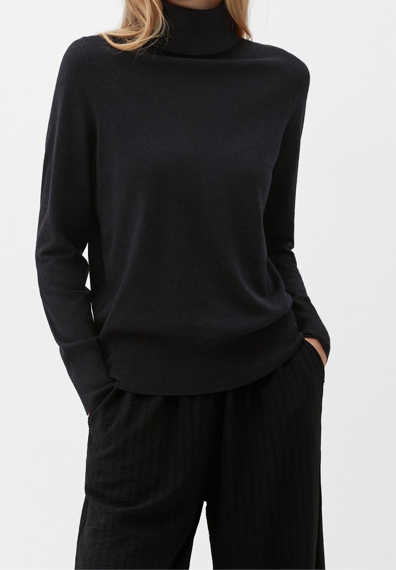 Pull à col roulé bleu marine en tissu doux, doté de manches longues, d'une coupe décontractée et d'un ourlet côtelé. Associé à un pantalon noir texturé.