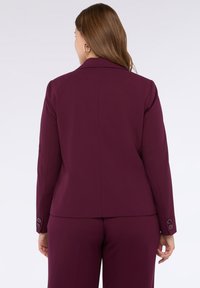 Burgundský blazer s přiléhavým střihem, dlouhými rukávy, klopami a knoflíkovými detaily na manžetách. Hladká, strukturovaná tkanina.