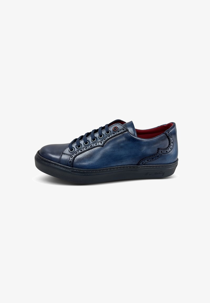 Zapatilla de cuero en azul marino con un acabado suave, acentos de costura en contraste, suela de goma negra y forro interior rojo.