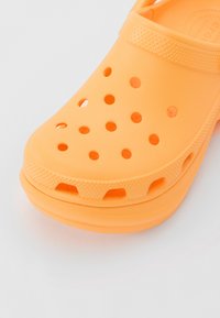 Sabot en caoutchouc orange avec des trous d'aération pour la respirabilité ; dessus texturé et sangle ; bout rond et semelle intérieure ergonomique pour le confort.