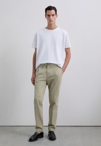 Camiseta blanca de manga corta combinada con pantalones beige claros que cuentan con una cintura ajustable con cordones; unos mocasines negros completan el atuendo.