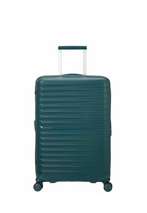 Valigia rigida color verde petrolio scuro con scanalature orizzontali, manico telescopico esteso e quattro ruote girevoli su sfondo bianco.