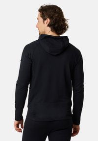 Felpa nera con maniche lunghe, tessuto texturizzato, cappuccio sul retro e caratteristiche regolabili. Design minimalista senza loghi o motivi visibili.