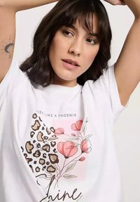 Biała koszulka z nadrukiem w motyw lamparta i kwiatów w odcieniach różu i zieleni, z napisem "Powstań jak feniks" w kolorze czarnym.