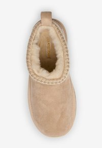 Chausson beige en daim doux, avec une doublure en peluche, un bord cousu et une petite languette à l'arrière pour un enfilage facile.